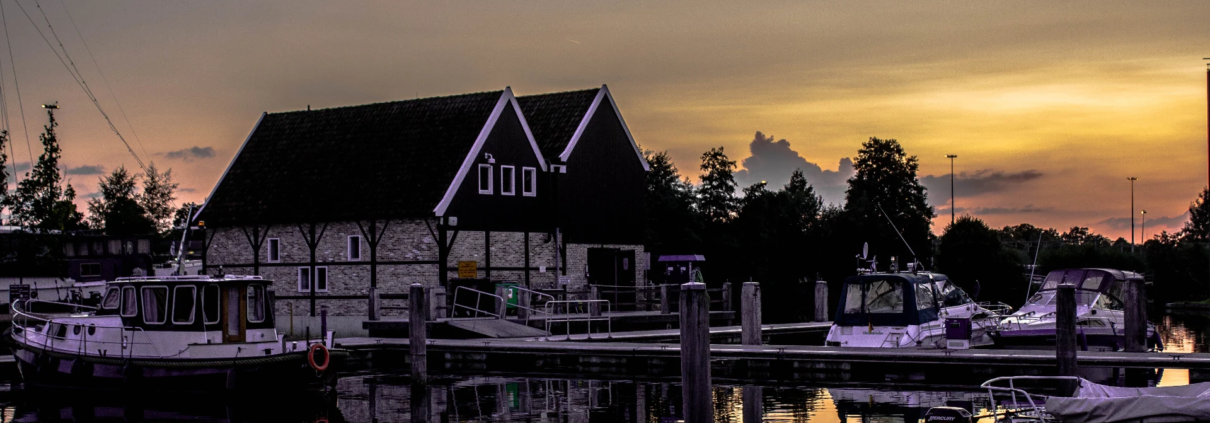 Boten aangemeerd in een jachthaven bij zonsondergang, met een traditioneel gebouw op de achtergrond.