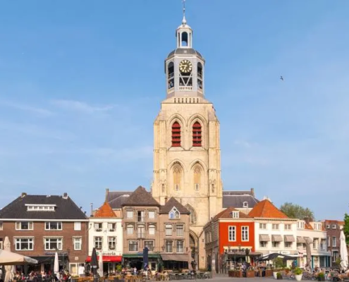 De toren van de Grote Kerk in Breda, omringd door historische gebouwen en terrassen op een zonnig plein.
