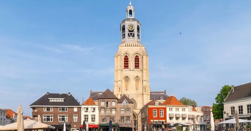 De toren van de Grote Kerk in Breda, omringd door historische gebouwen en terrassen op een zonnig plein.