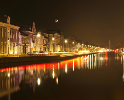 Verlichte grachtenpanden en reflecties in het water tijdens een heldere nacht in Leeuwarden.