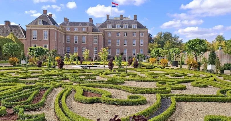 Barokke tuin met symmetrische hagen voor Paleis Het Loo in Apeldoorn, met Nederlandse vlag op het dak.